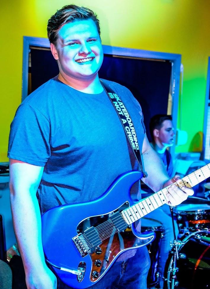 Calvin smiling while playing a blue electric guitar