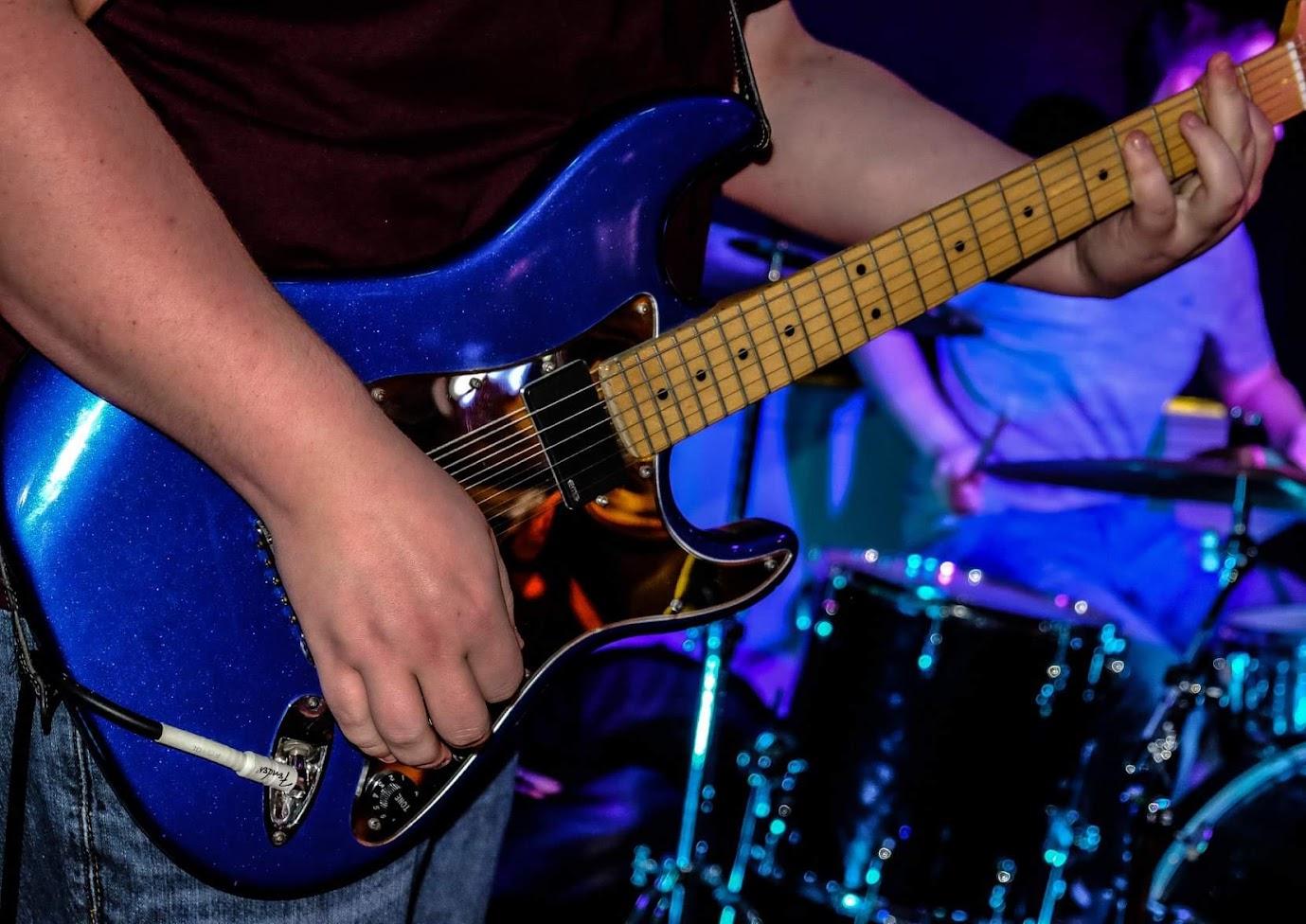 A close-up of Calvin’s blue electric guitar being played