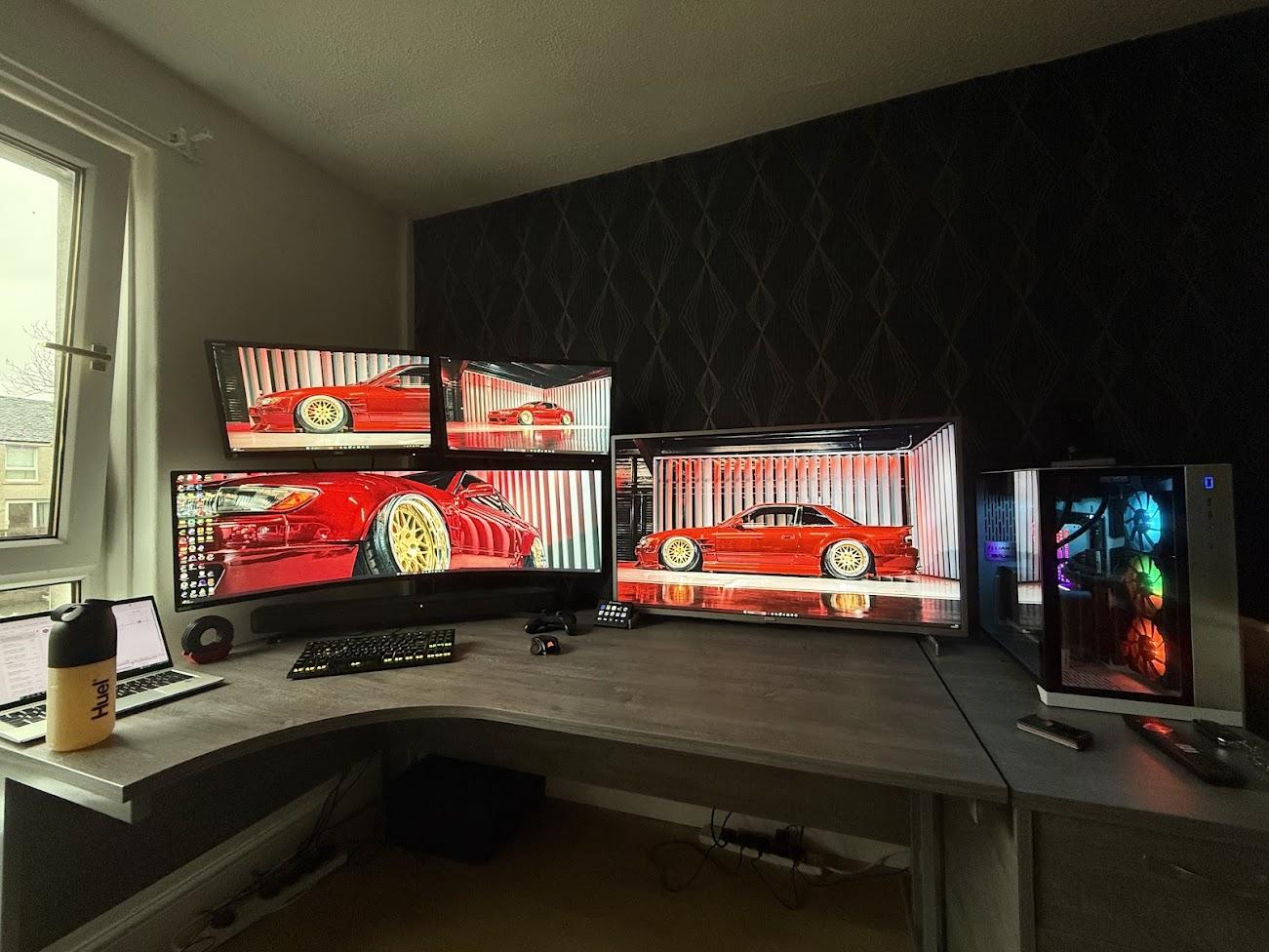 Calvin’s home desk with several monitors and a desktop computer in daylight